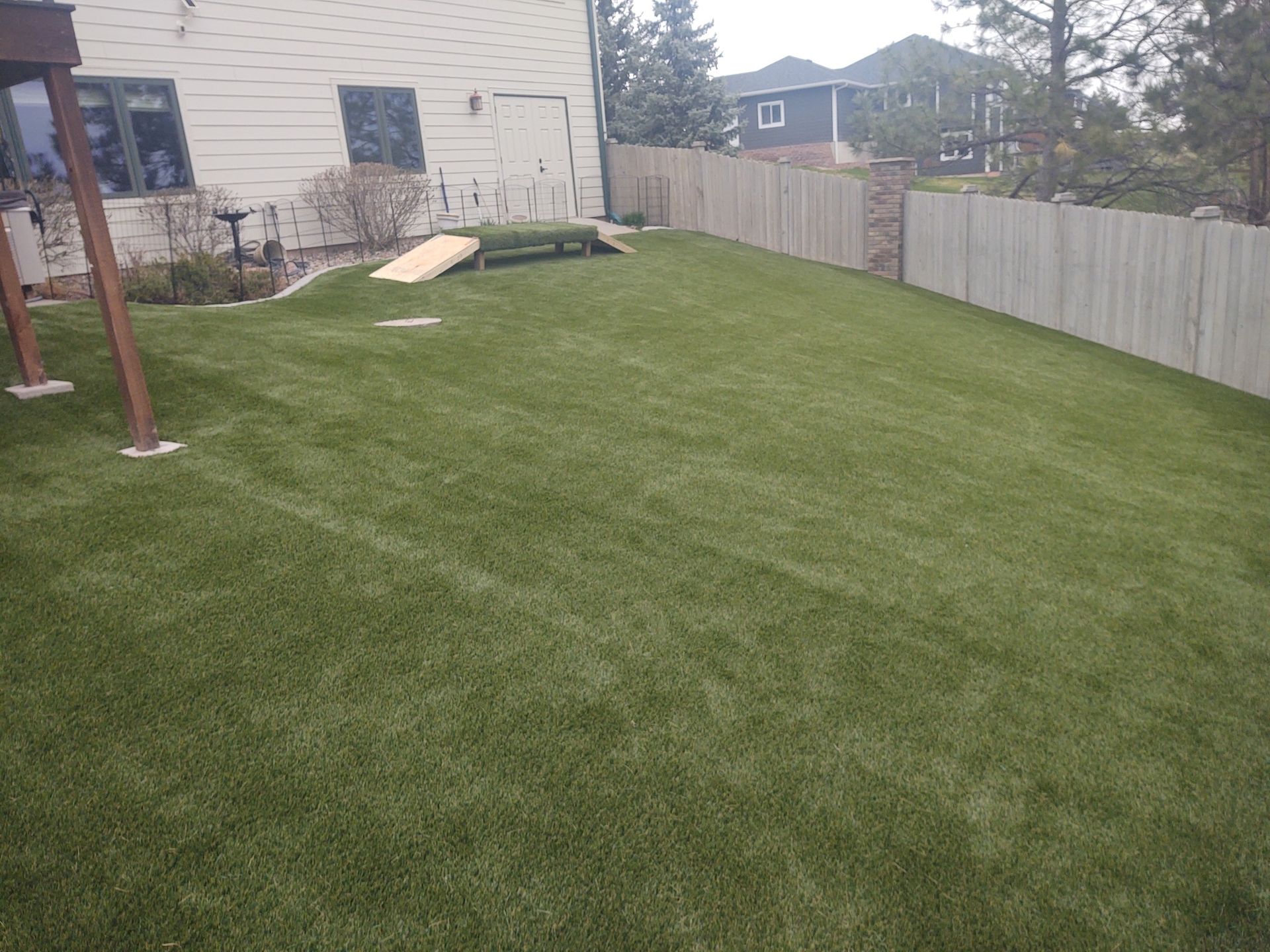 Backyard with green artificial turf, wooden fence, dog ramp, and house
