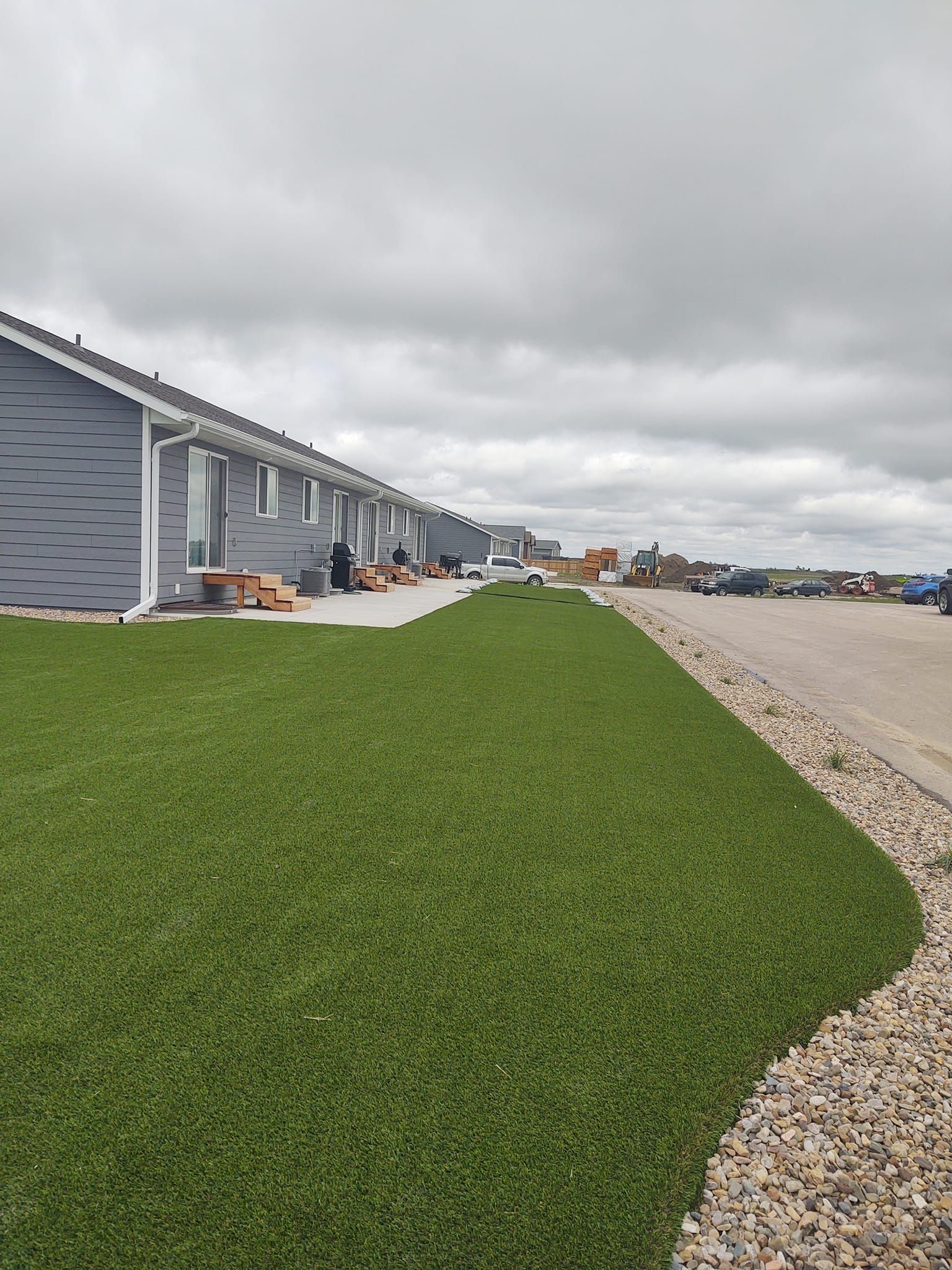 Row of modern buildings with gray siding, green lawn, gravel, and cloudy sky