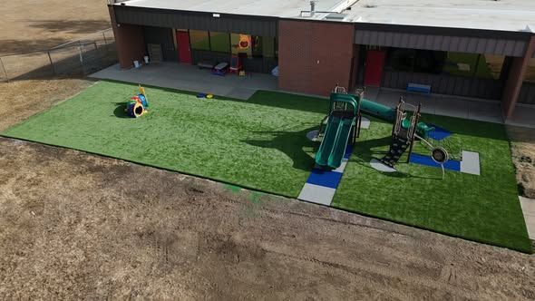 Playground with green turf, equipment, and a building in the background