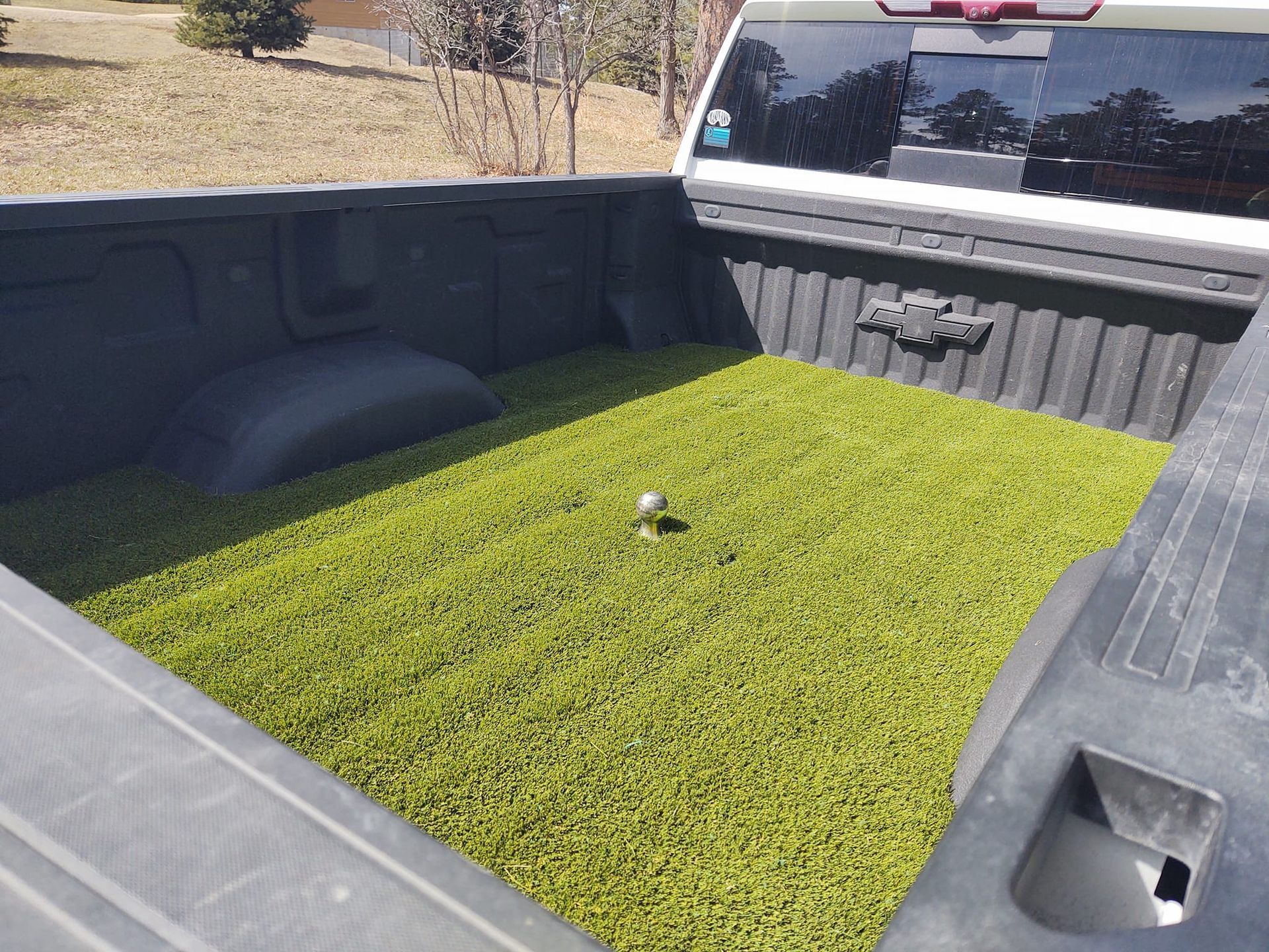 A truck bed lined with bright green artificial turf, featuring a central hitch ball in an outdoor setting.