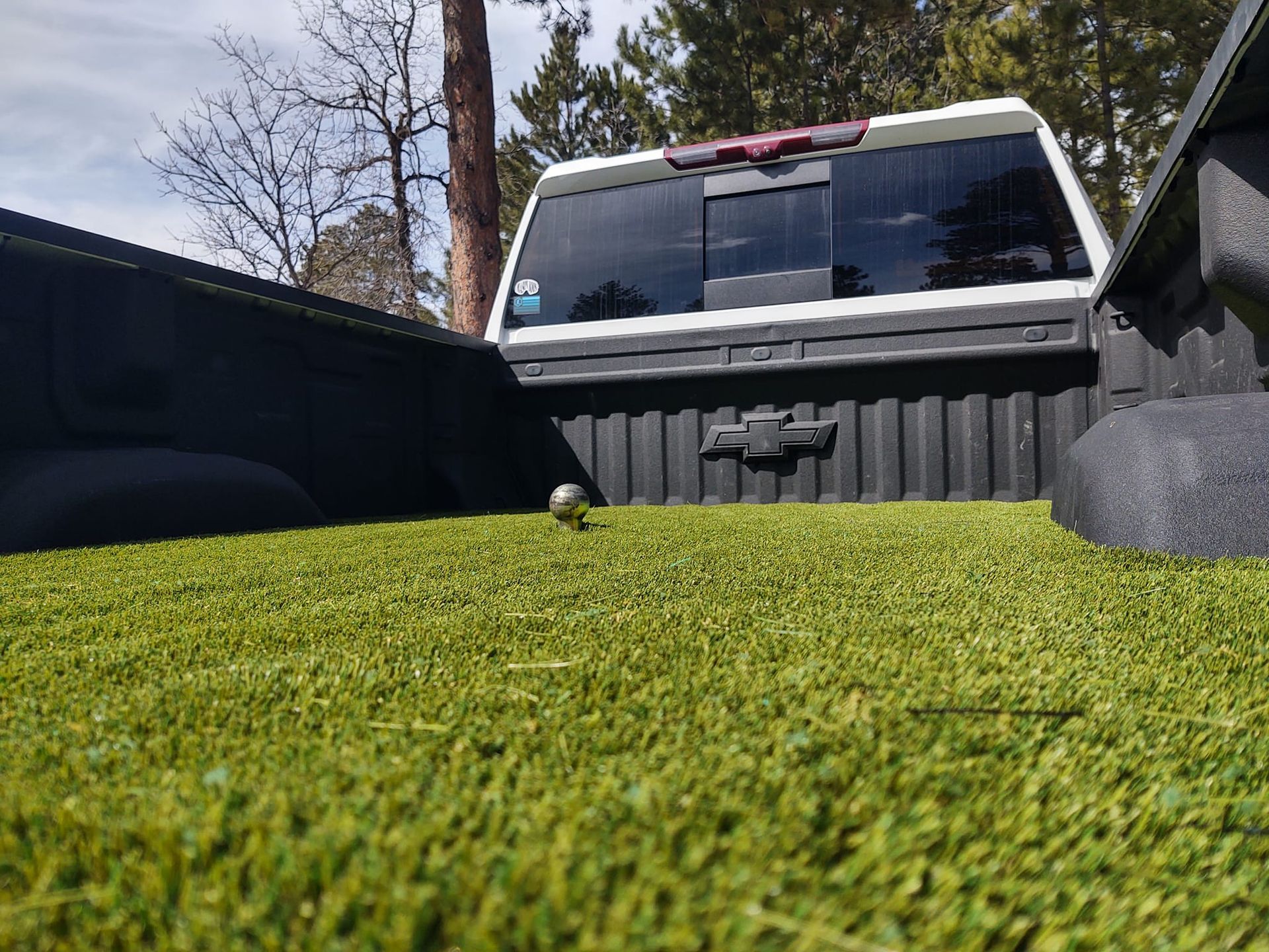 White pickup truck bed with green turf, a small silver ball, and the Chevrolet emblem