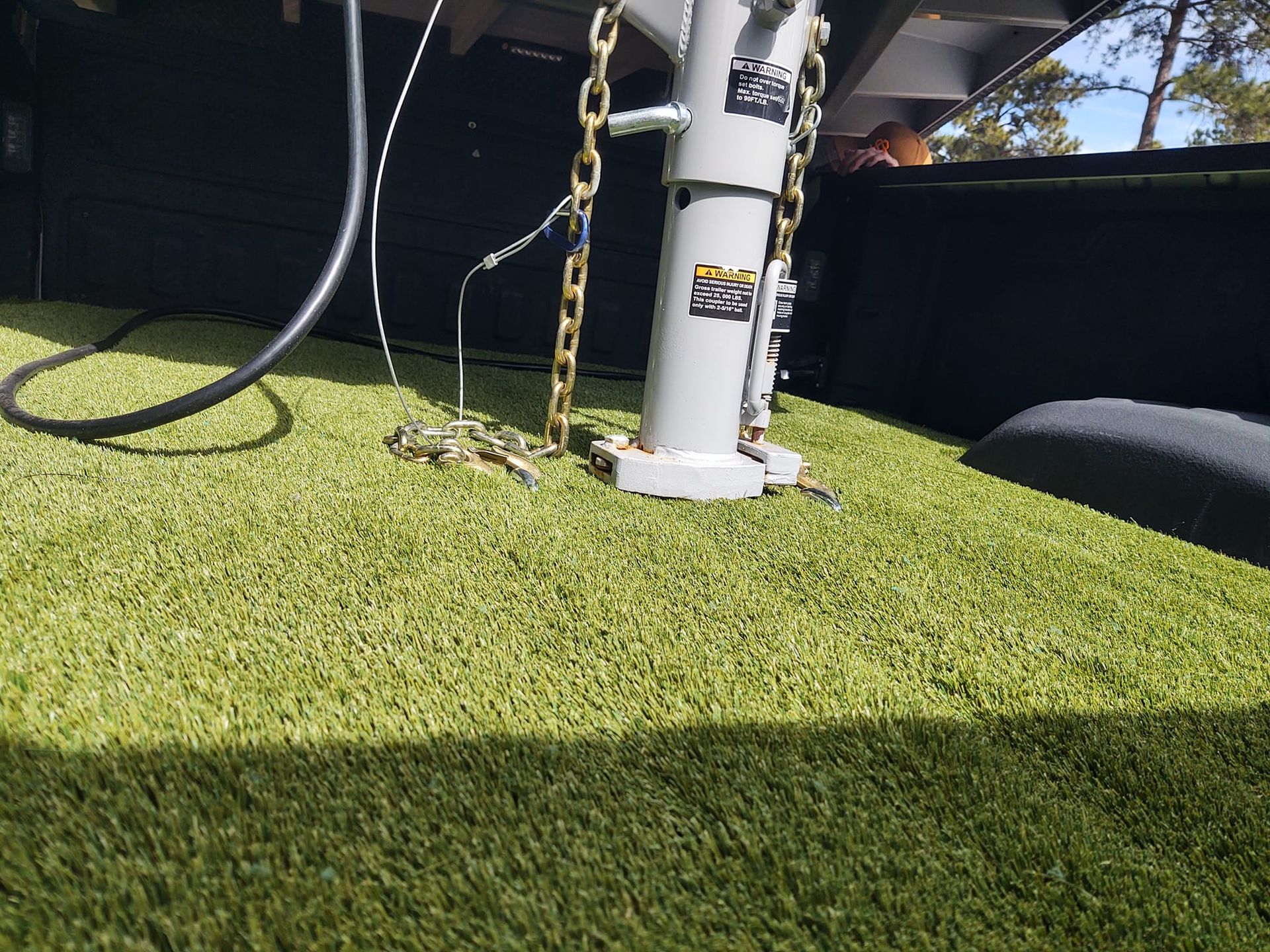 Truck bed with green turf, a gooseneck hitch, and safety chains