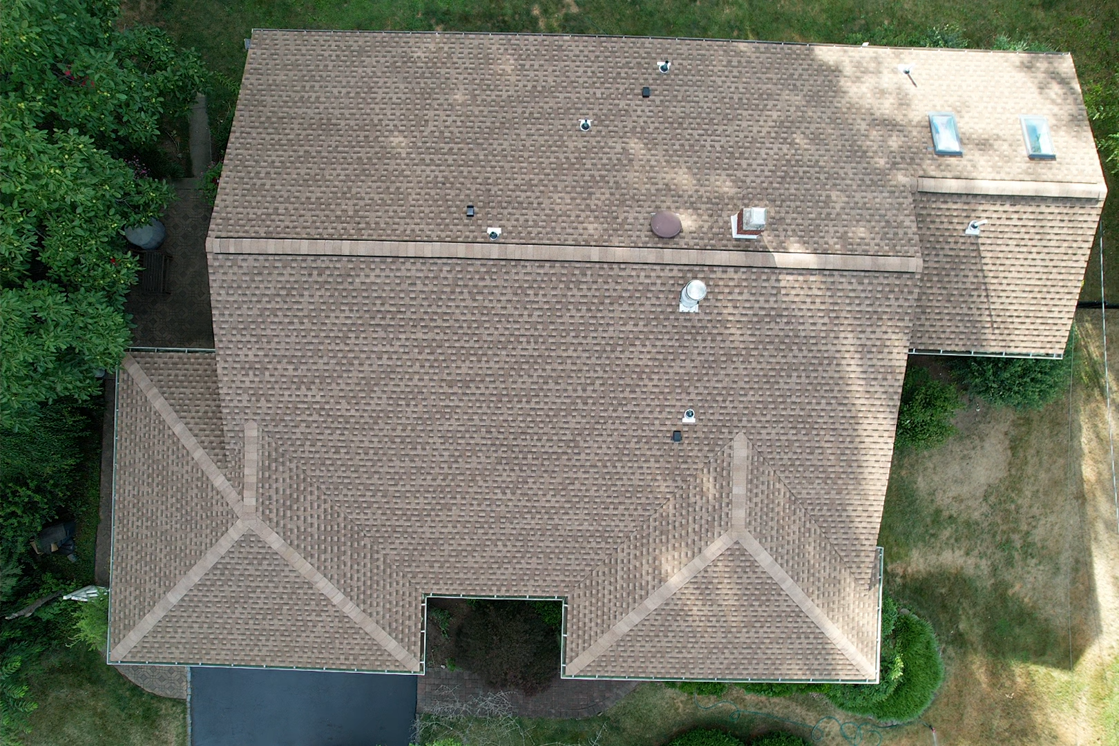 An aerial view of a house with a brown roof surrounded by trees