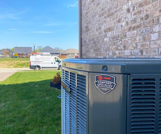 A gray air conditioner is sitting on the side of a brick building.