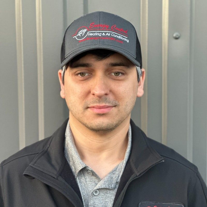 A man wearing a hat and a jacket is standing in front of a wall.