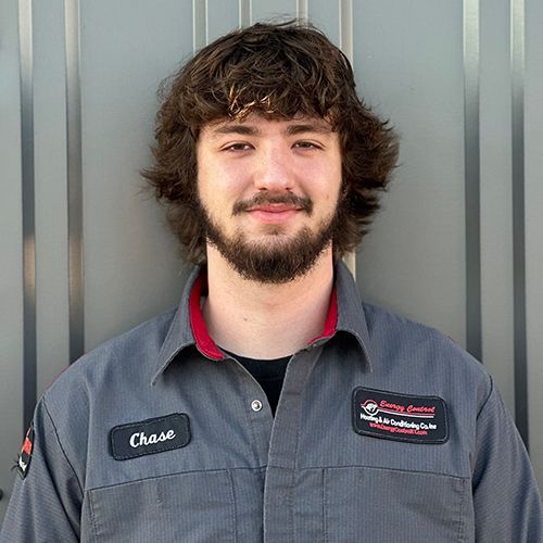 A young man with a beard is standing in front of a metal wall.