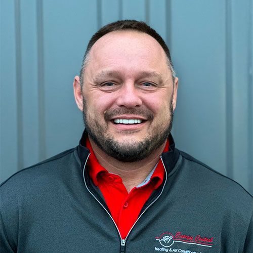 A man with a beard wearing a red shirt and a black jacket is smiling for the camera.