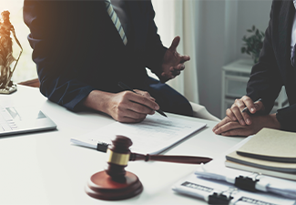 Lawyer meeting at desk with gavel, papers, and two people discussing a contract
