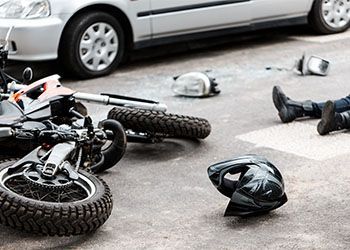 Motorcycle crash scene with fallen bikes, helmets, and debris on the road beside a parked car