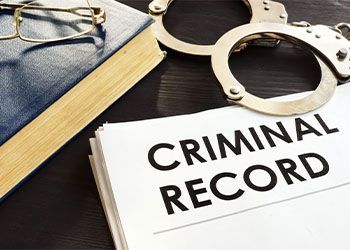 Handcuffs beside a book and a document labeled “CRIMINAL RECORD” on a desk