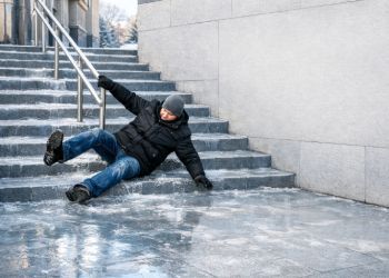 Person slipping on icy outdoor steps beside a building, bracing against the ground.