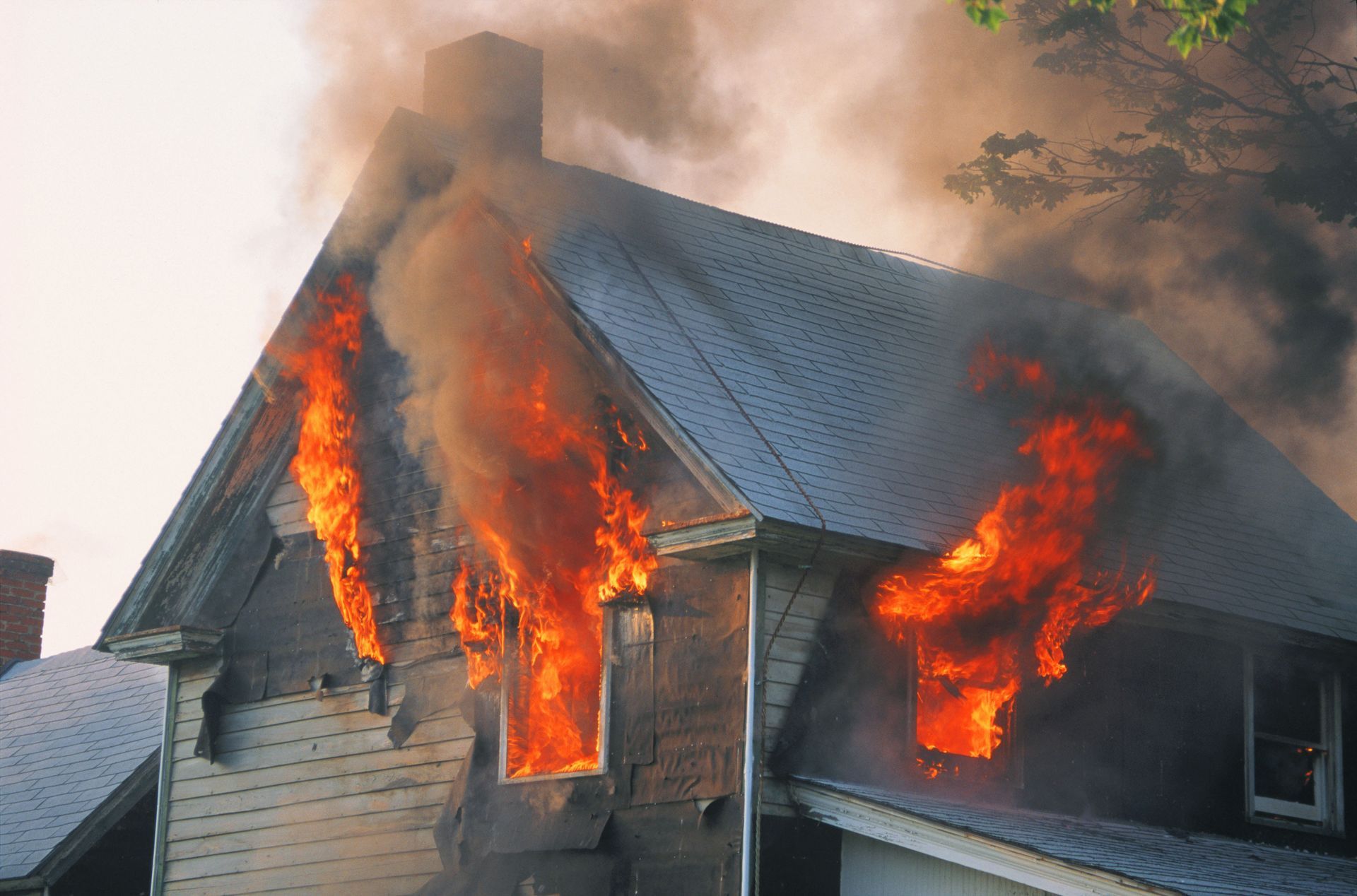 House fire with flames and smoke engulfing the roof and windows of a home