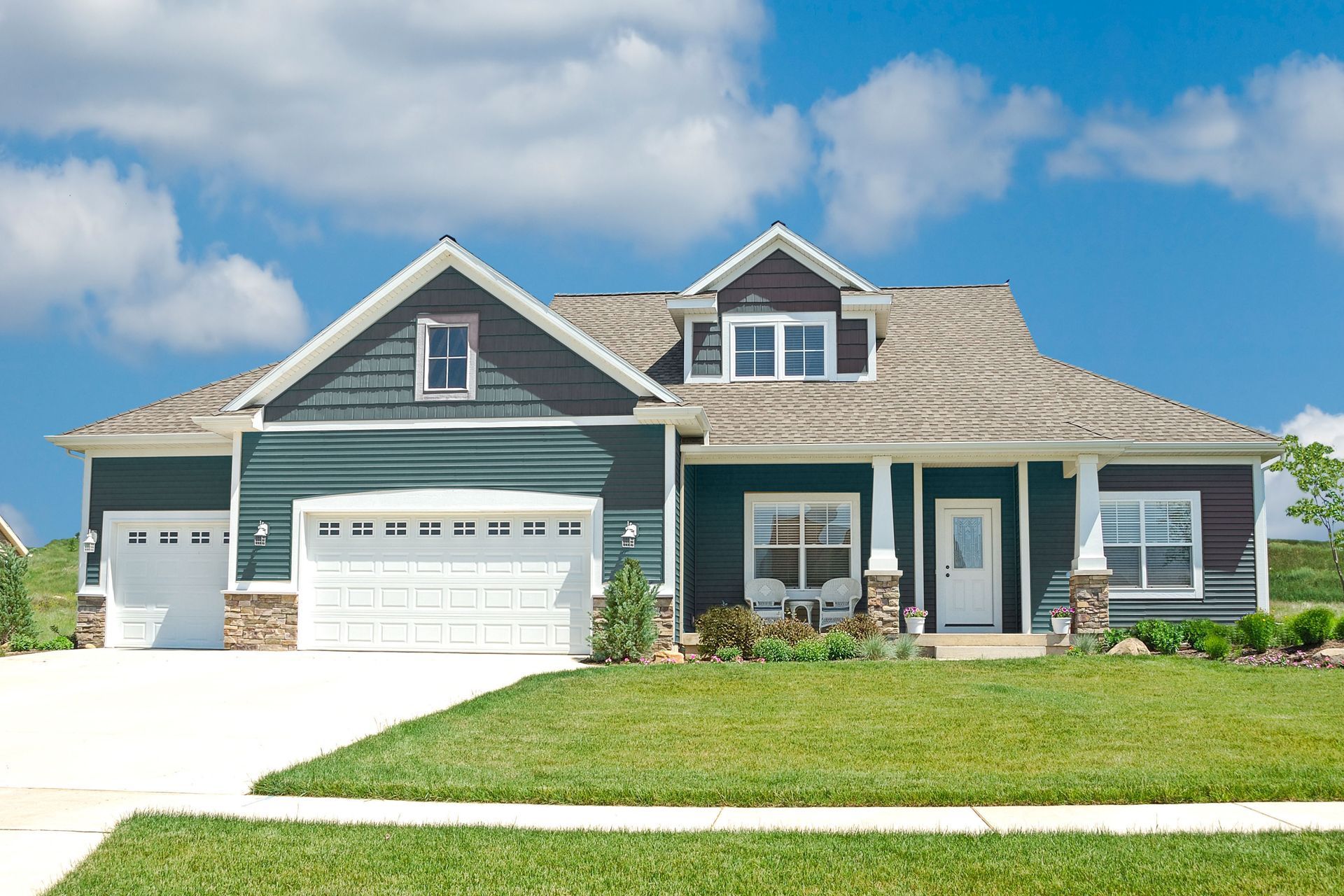 Suburban house with gray siding, three-car garage, and green lawn under a blue sky.