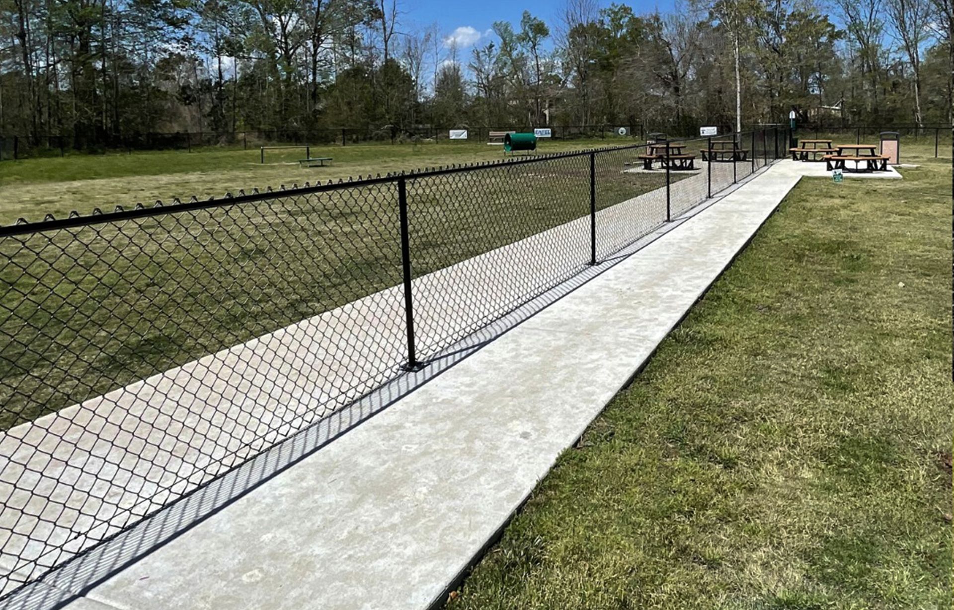 A chain link fence along a sidewalk in a park
