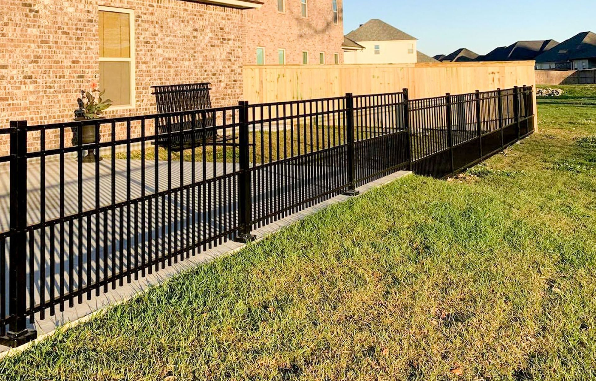 A black fence is surrounding a lush green lawn in front of a brick house.