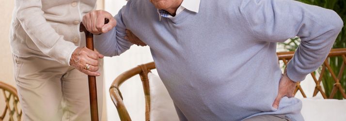 Person clutching lower back while standing near another person with a cane indoors