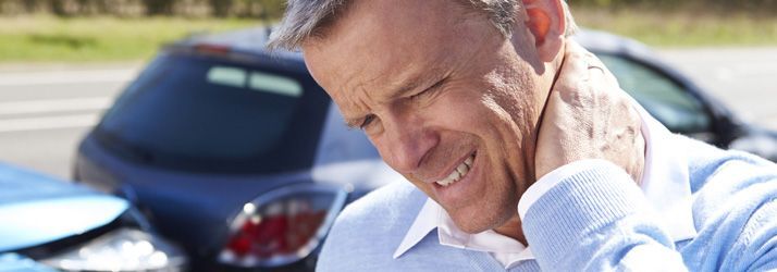 Man clutching his neck in pain beside a parked car outdoors