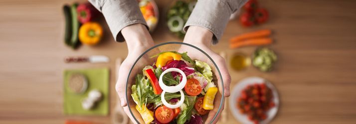 Hands holding a bowl of colorful salad with vegetables and onions on a wooden table