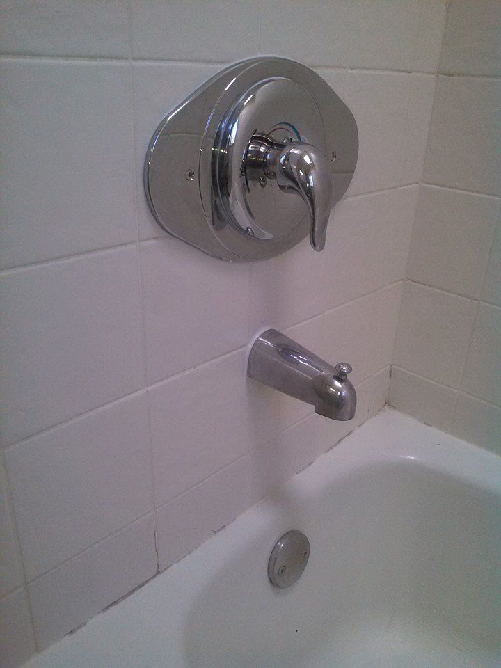 Chrome bathtub faucet with lever handle, attached to white tile wall above a white bathtub.