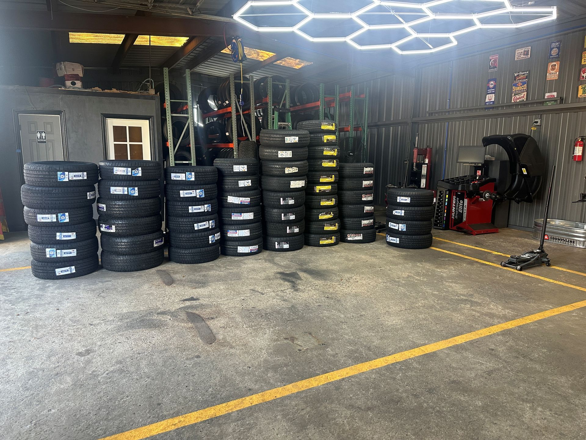 Indoor tire shop with stacks of racing tires, a red tool cart, and bright hexagonal ceiling lights.