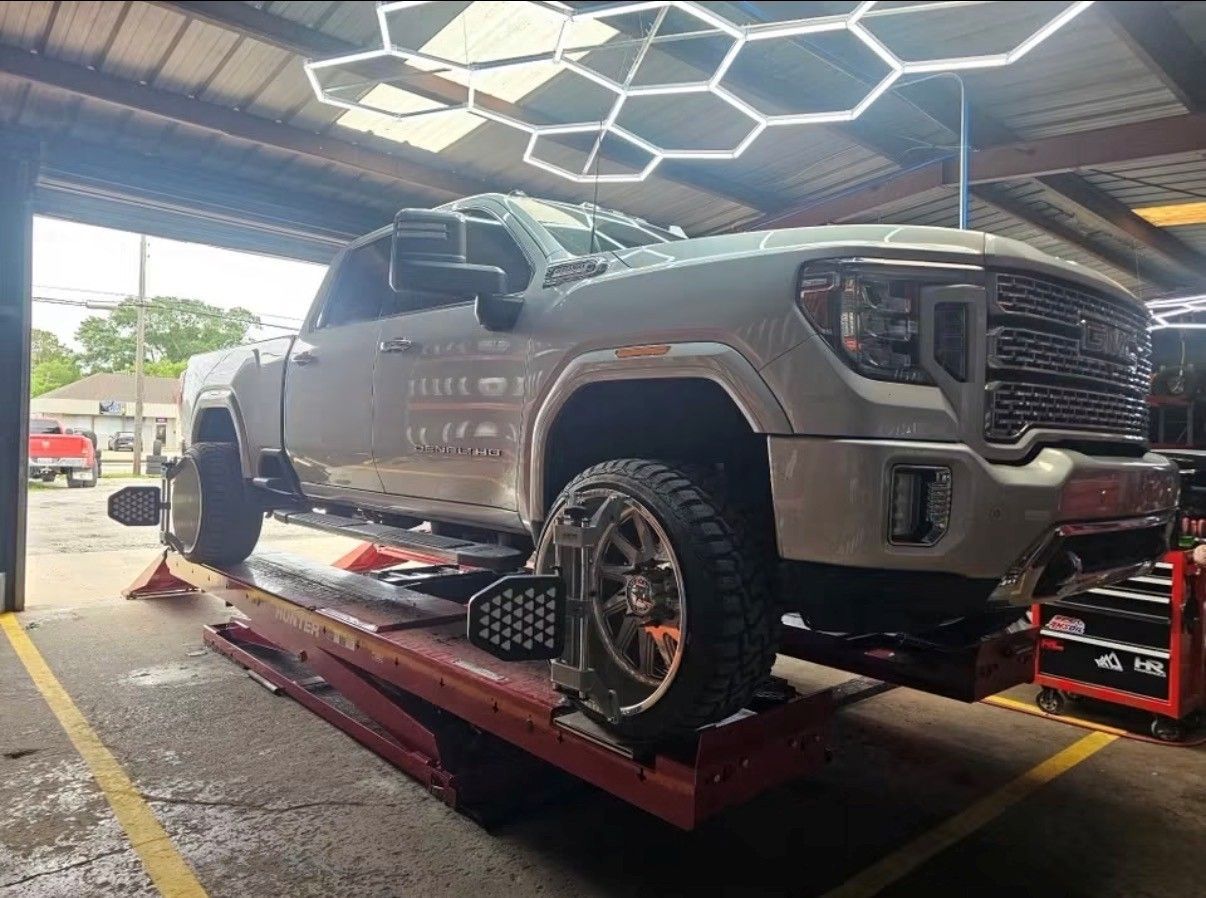 Silver lifted pickup truck on a red car lift inside an auto shop with hexagon ceiling lights