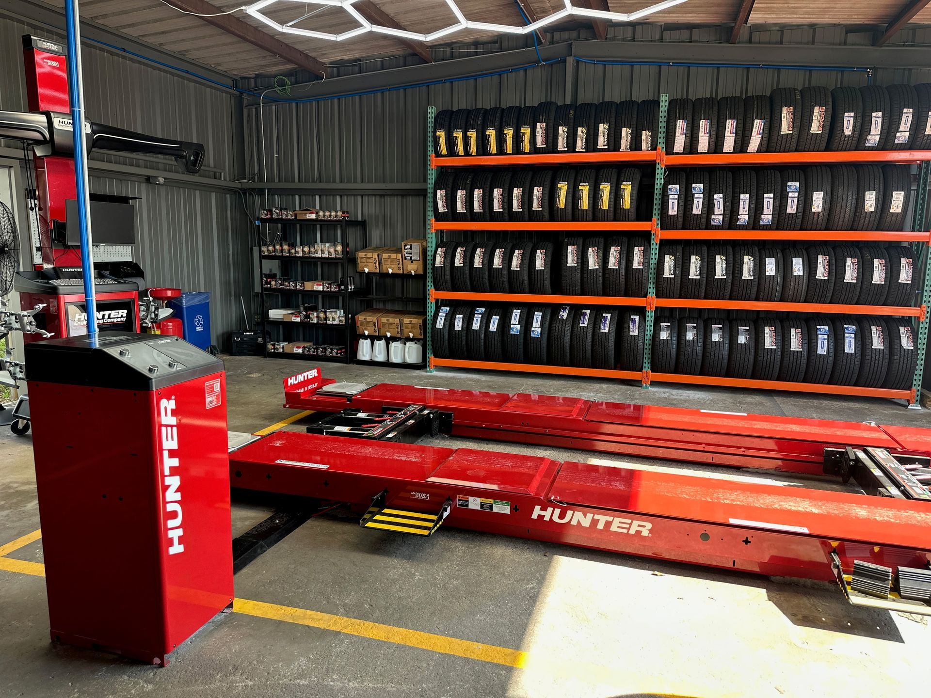 Red car lift in a garage showroom with shelves of oil bottles and a red HUNTER service machine