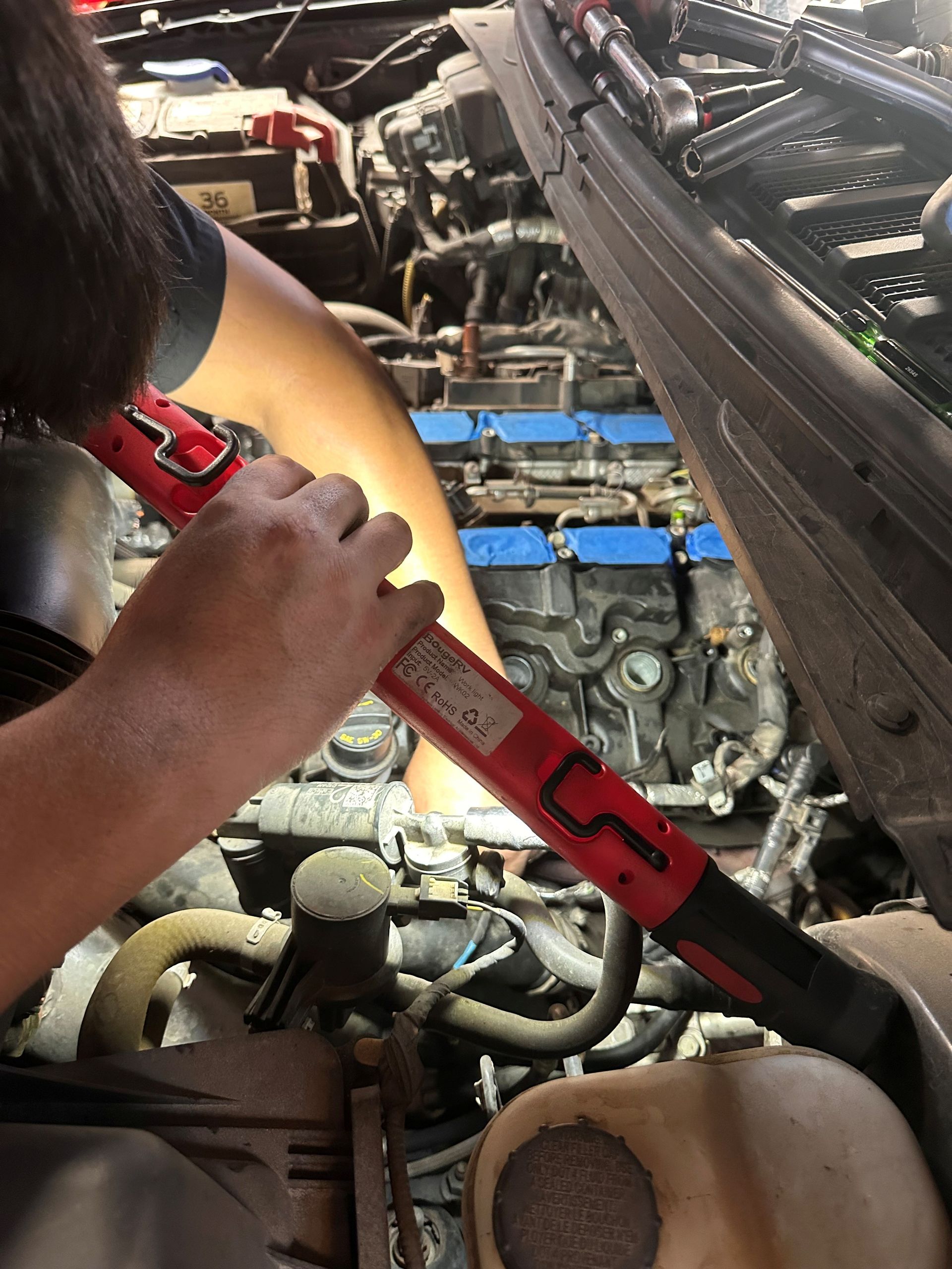 Person tightening a red strap in a car engine bay with blue components underneath.
