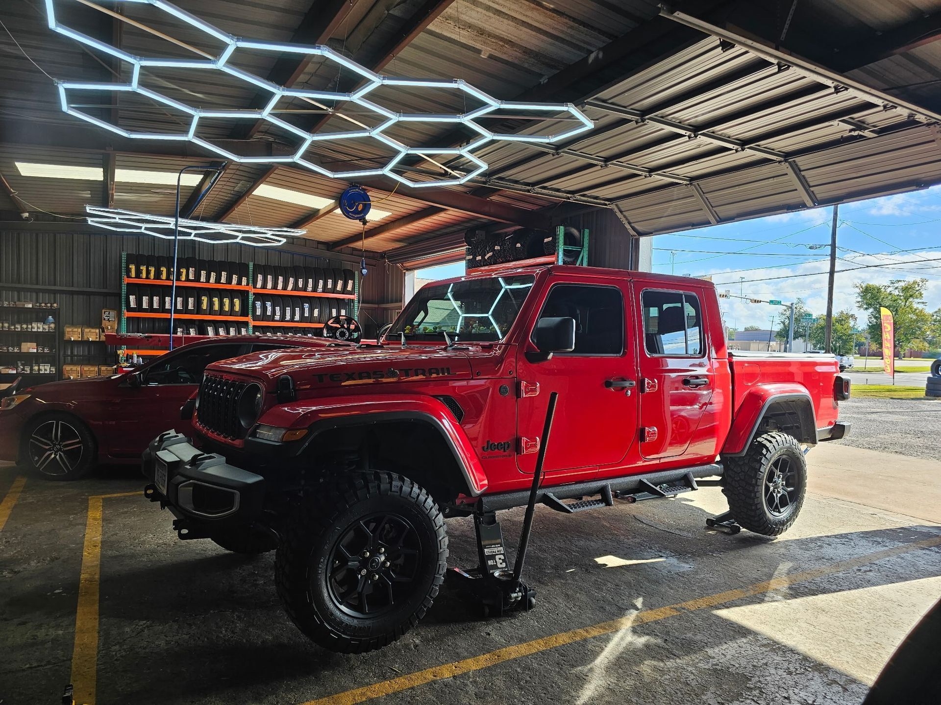 Red lifted pickup truck parked under a canopy with hexagon lights, viewed from the front-left.