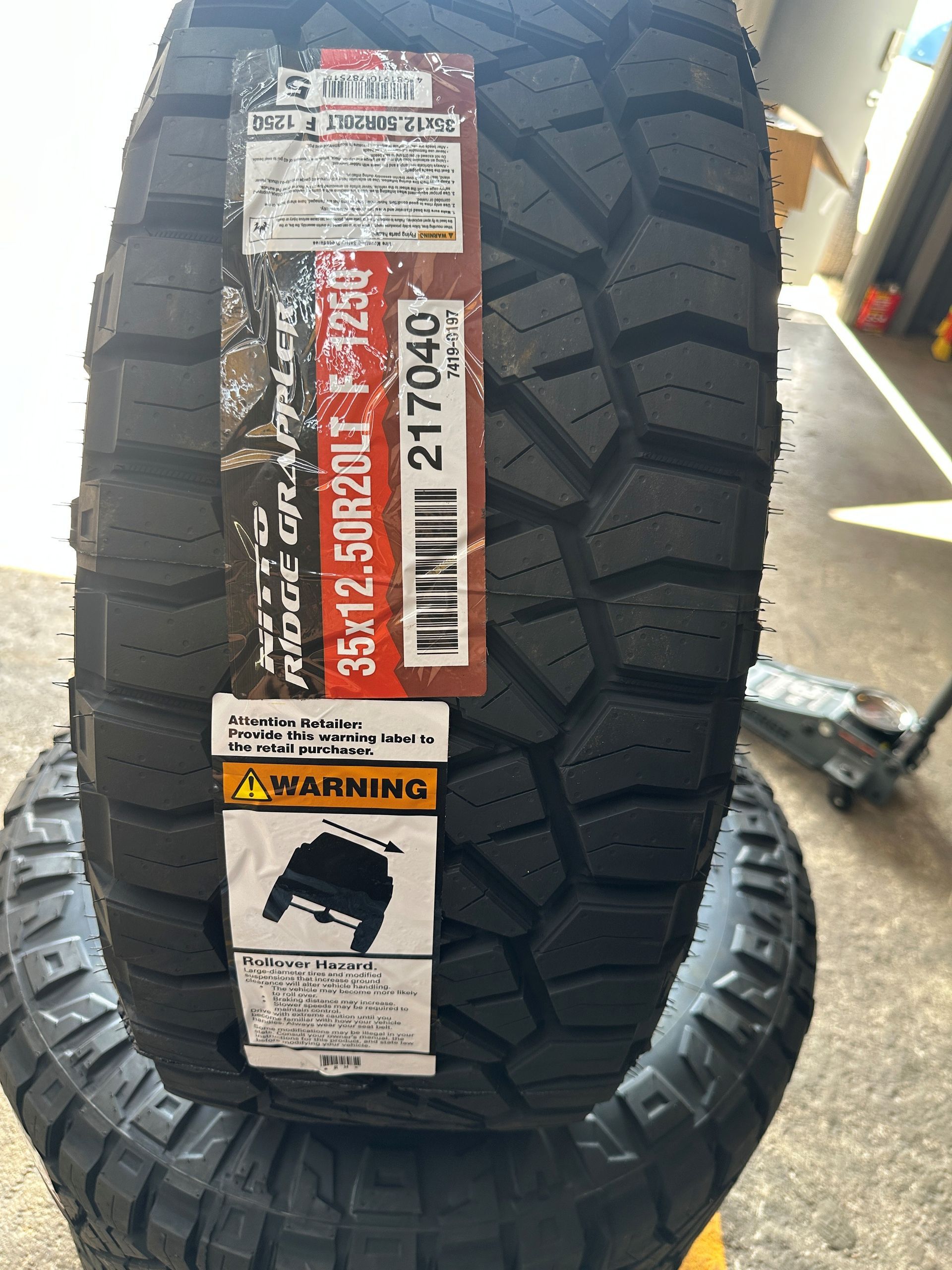 Two stacked black off-road tires with labels, shown in a store aisle.