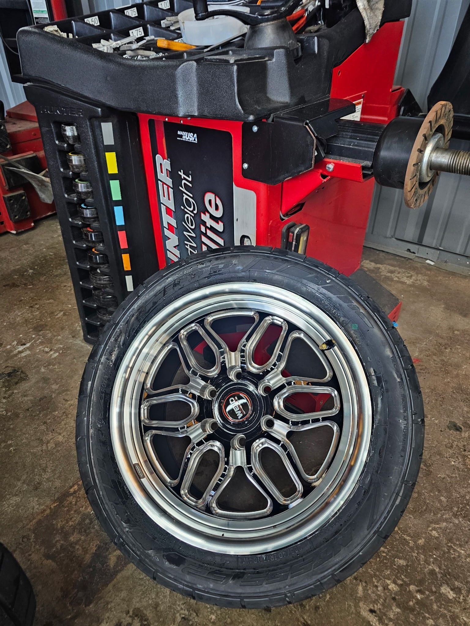 Racing car wheel with chrome rim mounted beside a red-and-black chassis in a garage
