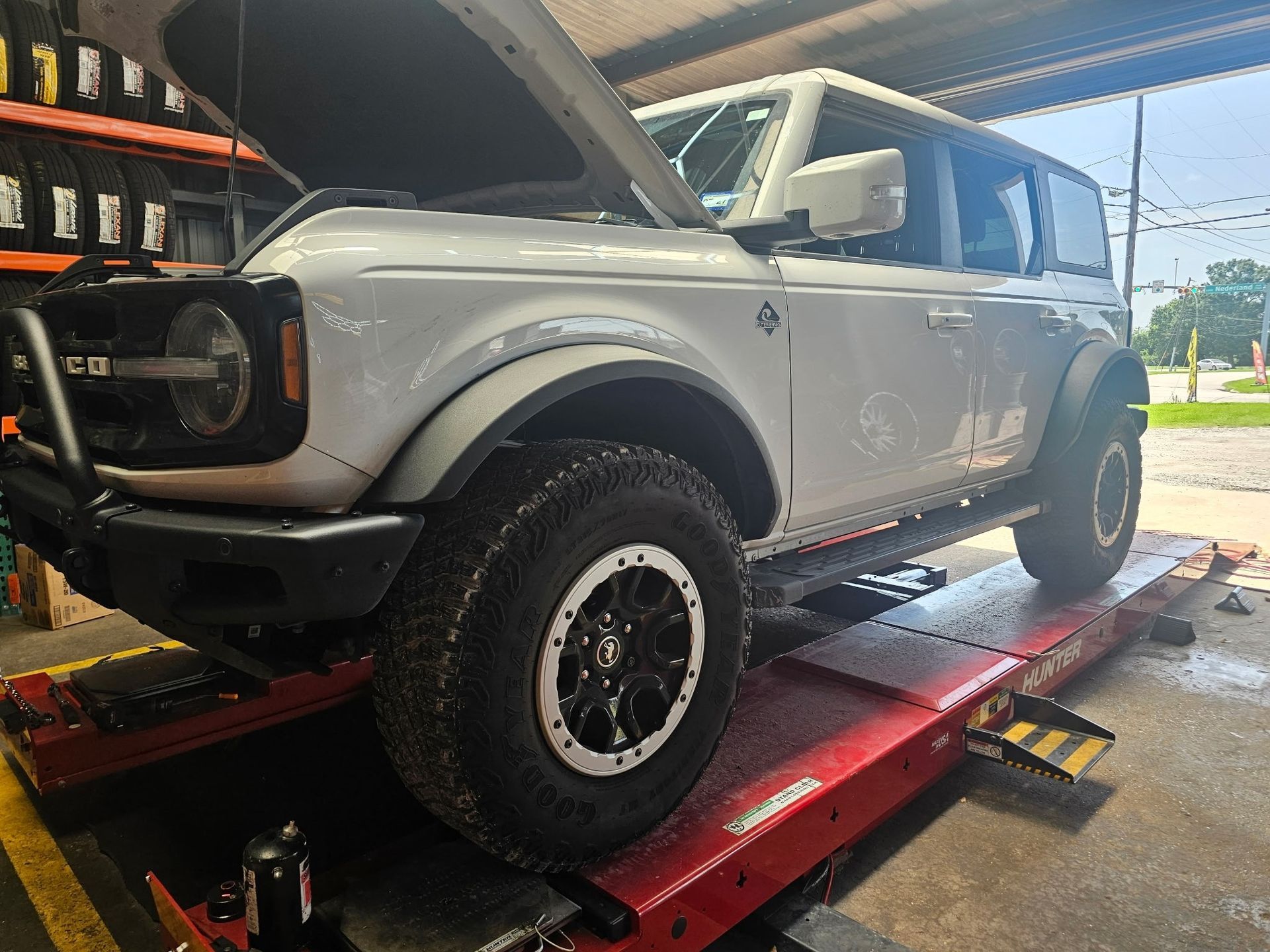 Silver SUV on a red car lift in a garage, hood open and front wheel visible.