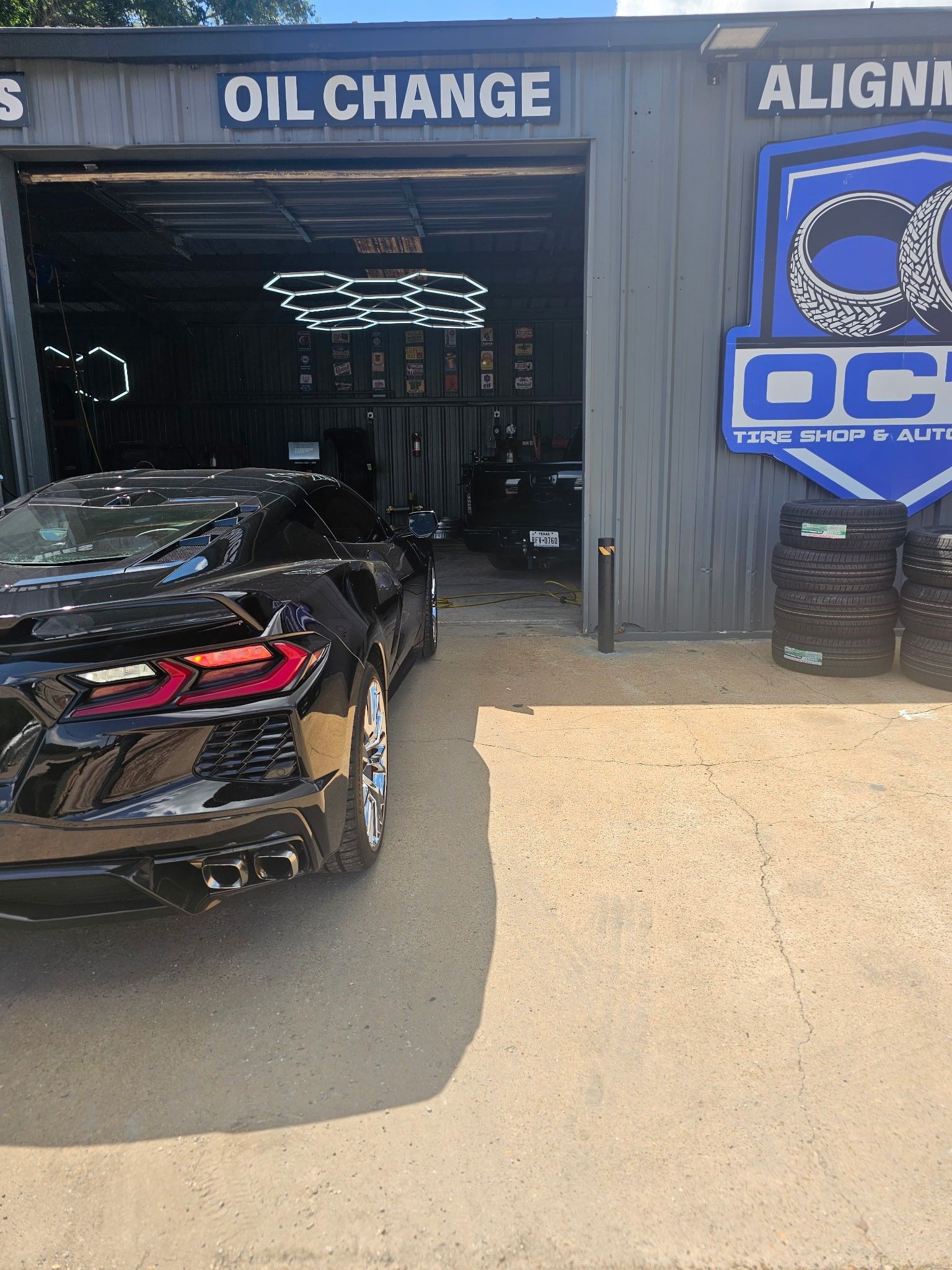 Black sports car parked outside an auto shop labeled “Oil Change” and “Alignment.”