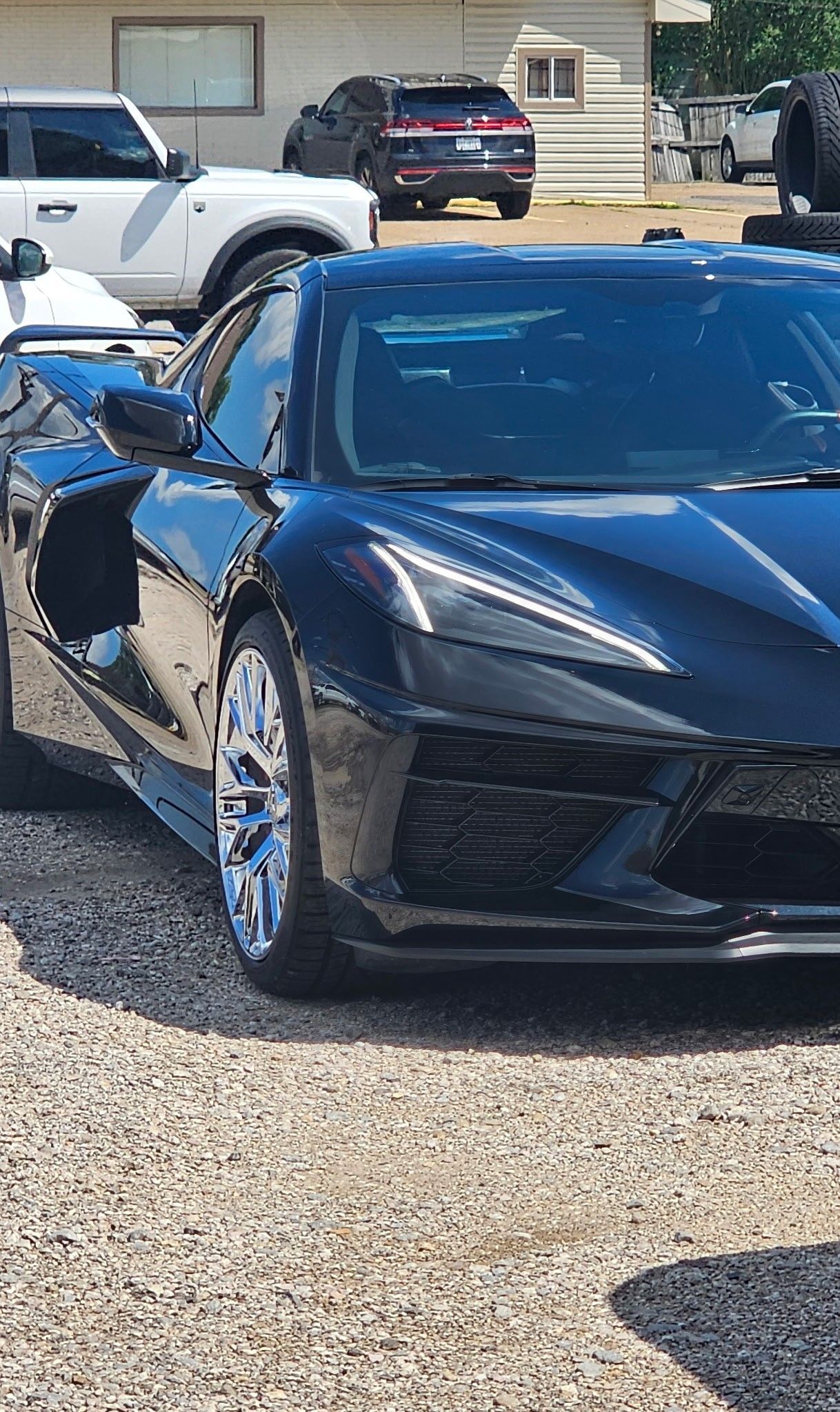 Black sports car parked on gravel lot with a white truck and other vehicles in the background