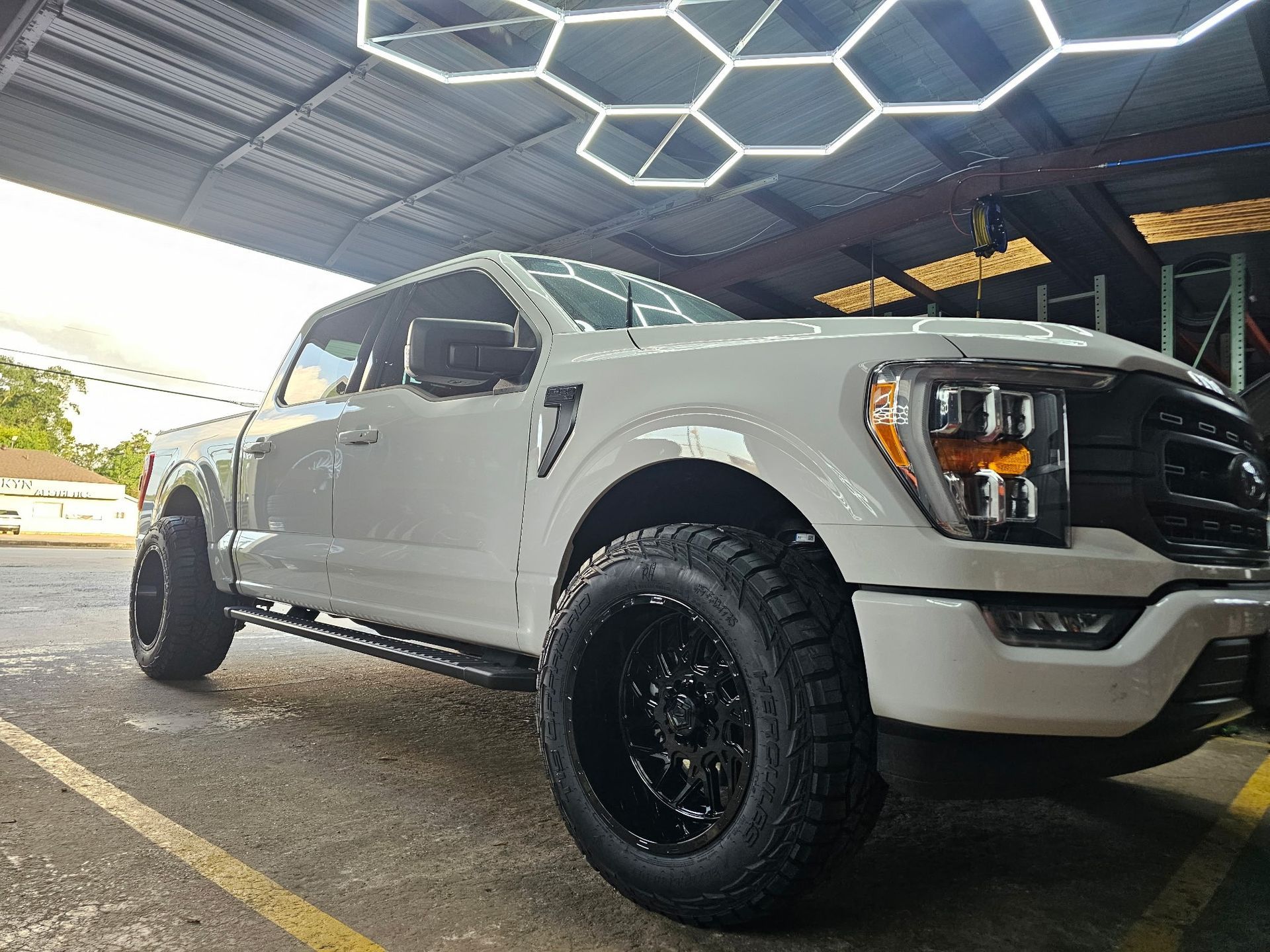 White lifted pickup truck with black wheels parked under a geometric-lit canopy
