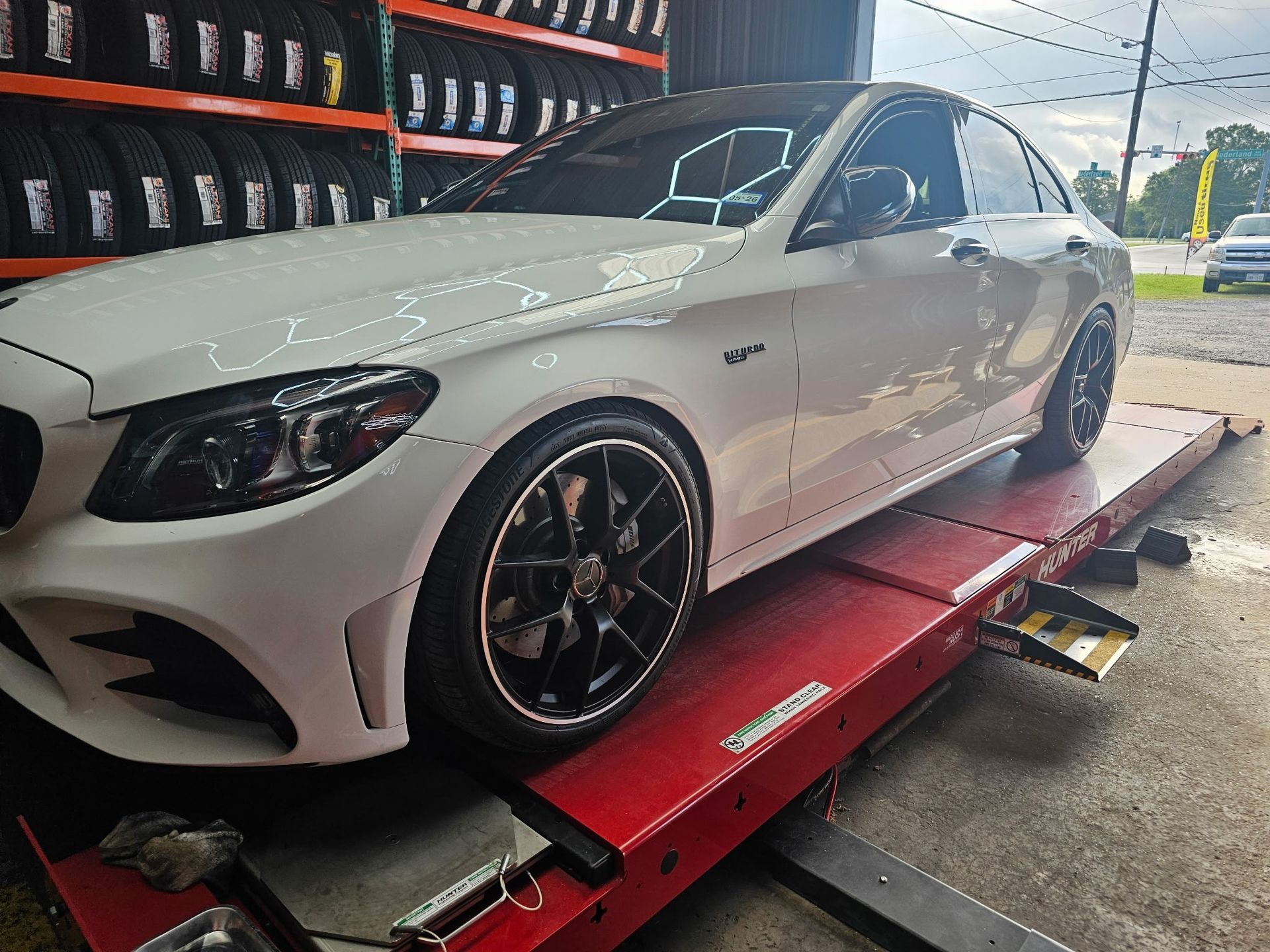 White Mercedes sedan on a red hydraulic car lift in an auto shop, side view