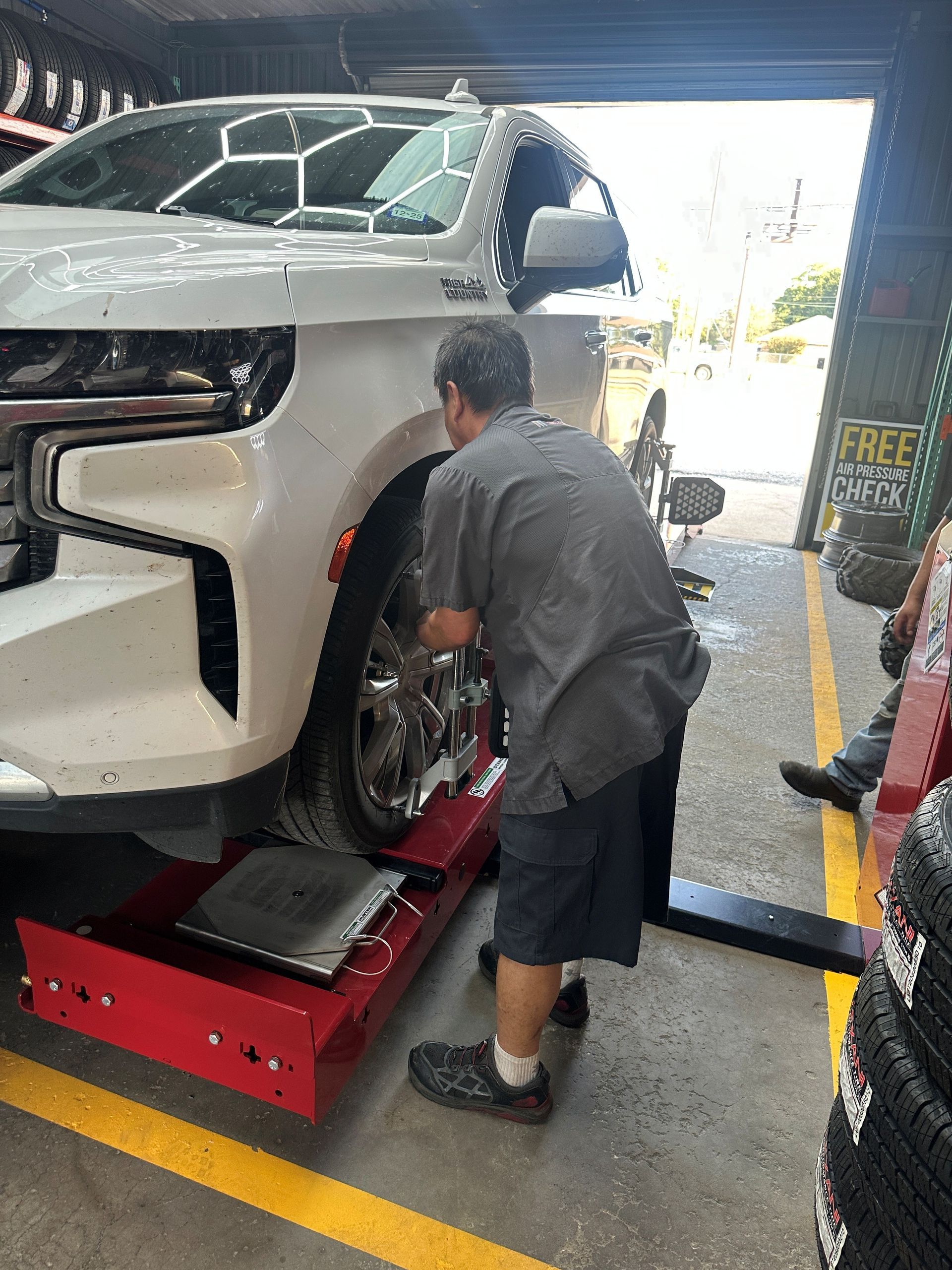 Mechanic working on a white SUV raised on a red lift in an auto shop.