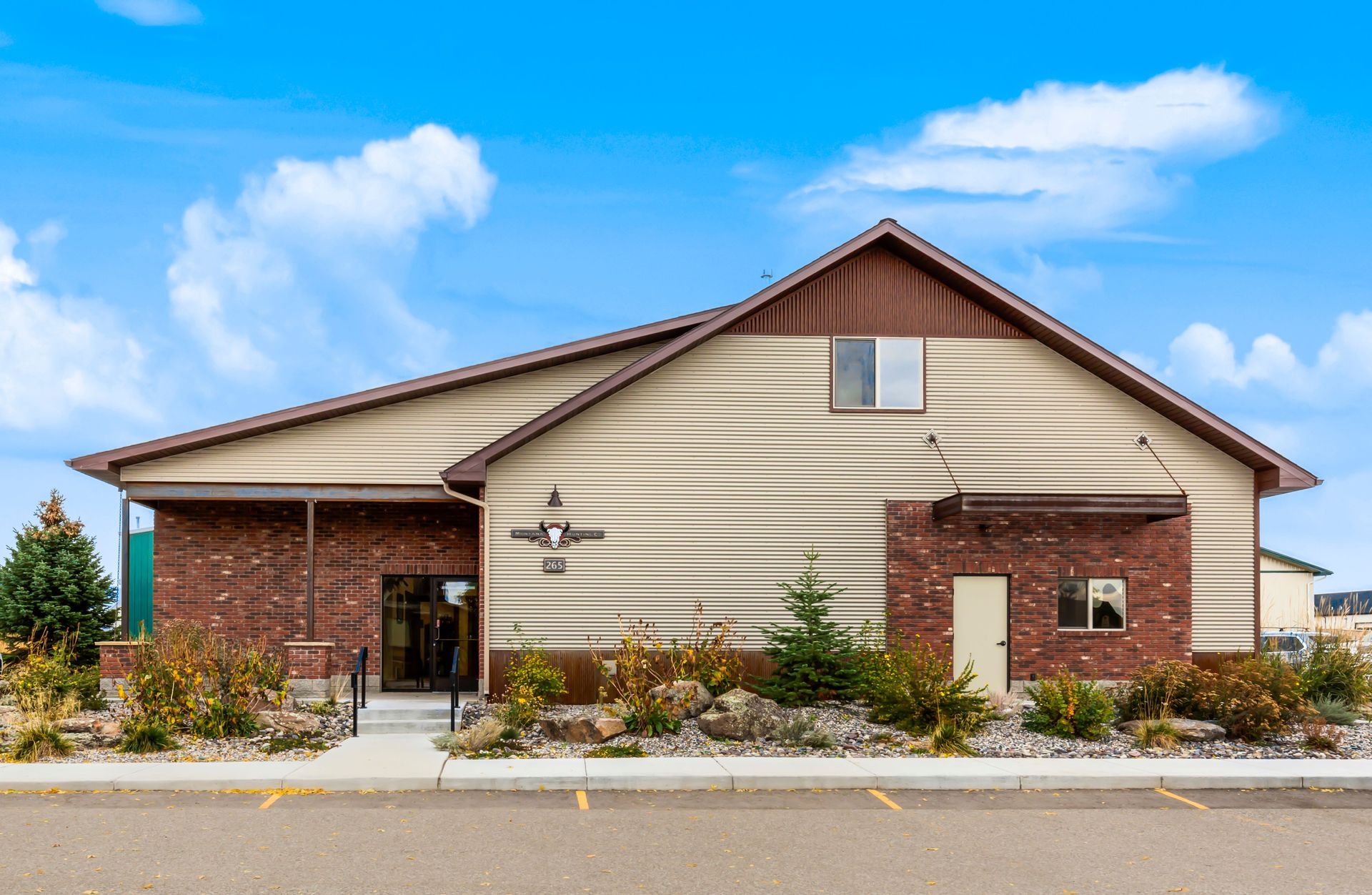 A modern, one-story commercial building with beige siding, brick accents, a gabled roof, and a parking lot in front.