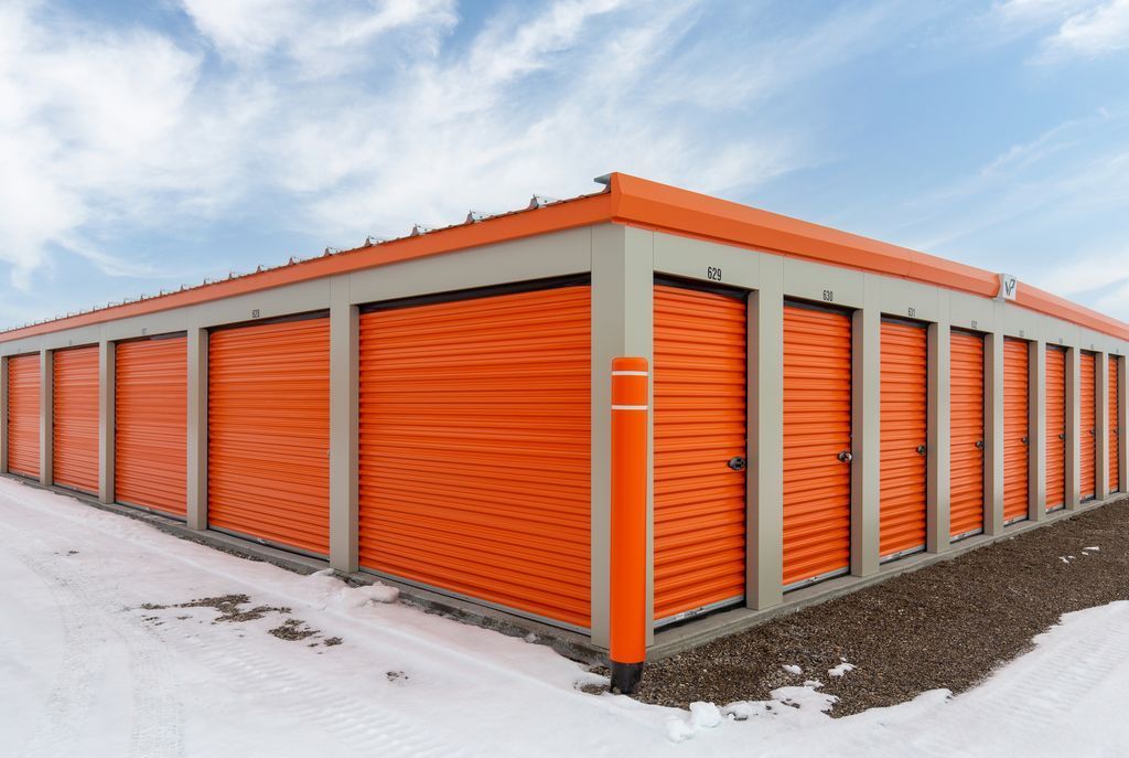A row of orange storage unit doors on a light-colored building set against a blue, cloudy sky with snow on the ground.