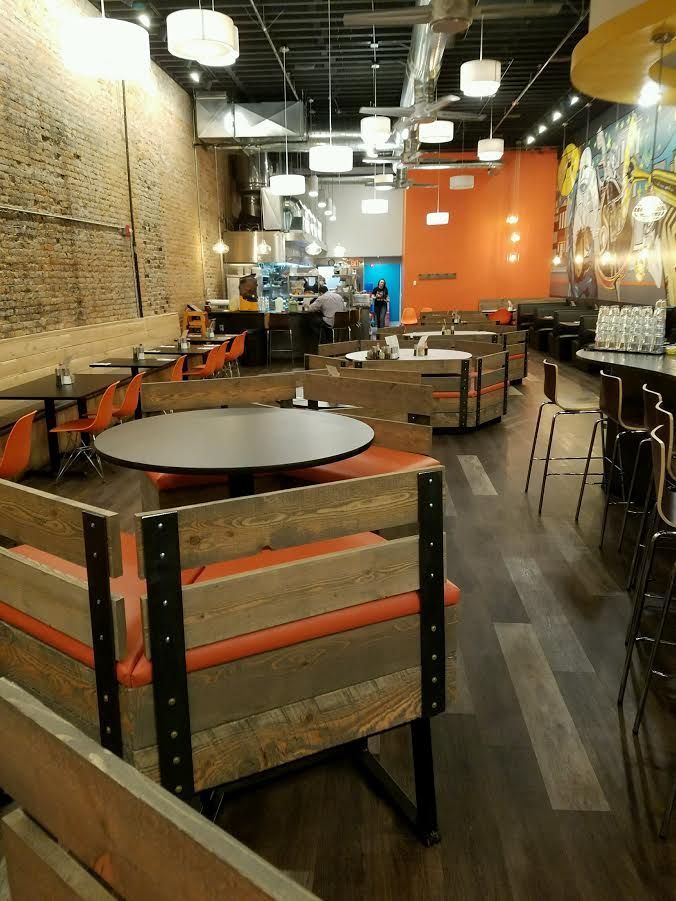 Empty restaurant interior with wooden booths, orange accents, brick wall, and modern overhead lighting.
