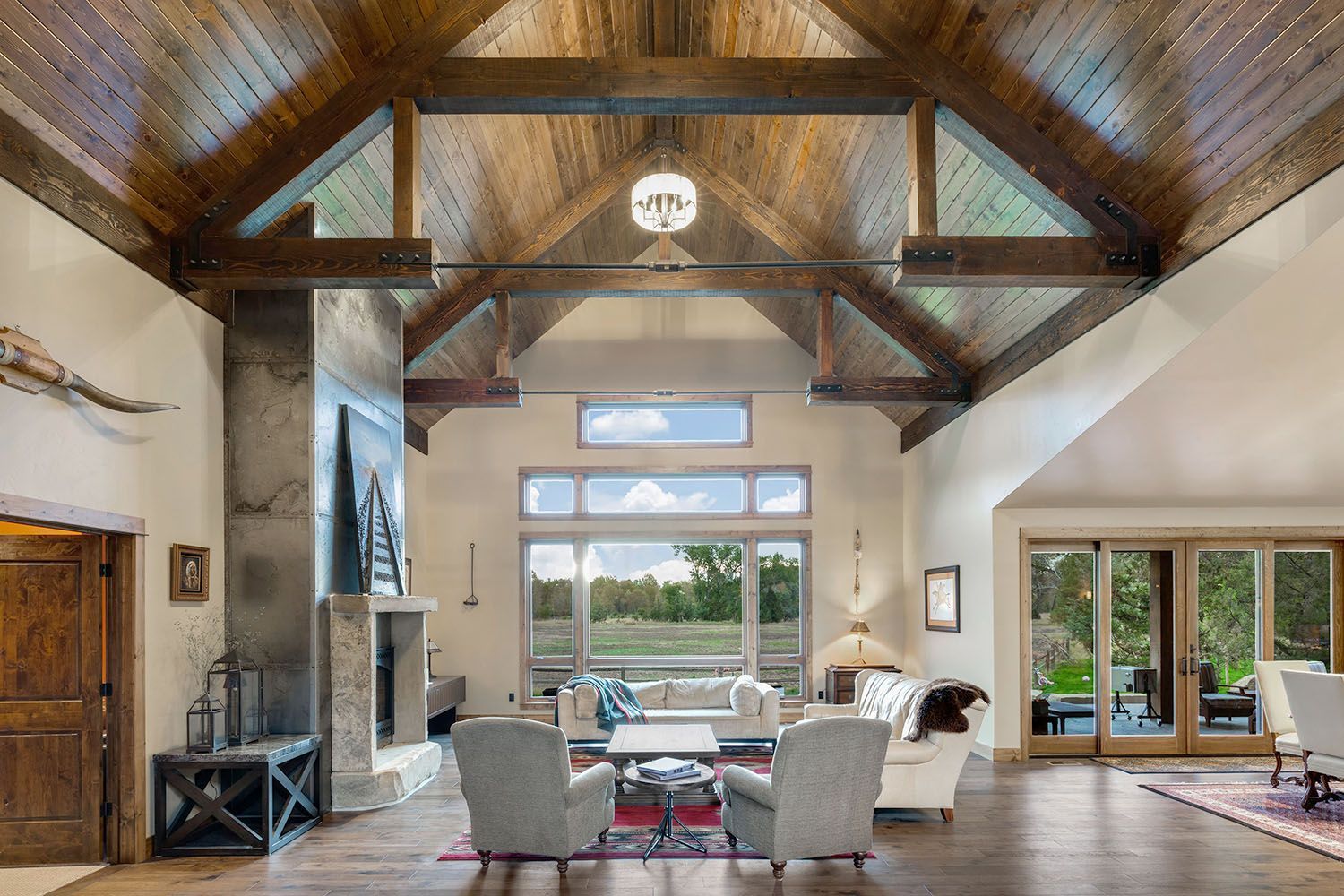 Spacious living room with a vaulted wood-paneled ceiling, exposed beams, stone fireplace, and floor-to-ceiling windows
