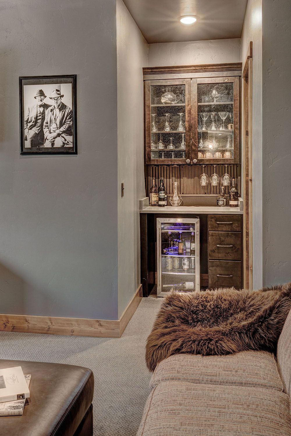 A built-in wet bar with dark cabinets, glass doors, and a small refrigerator, situated in a cozy room with a sofa