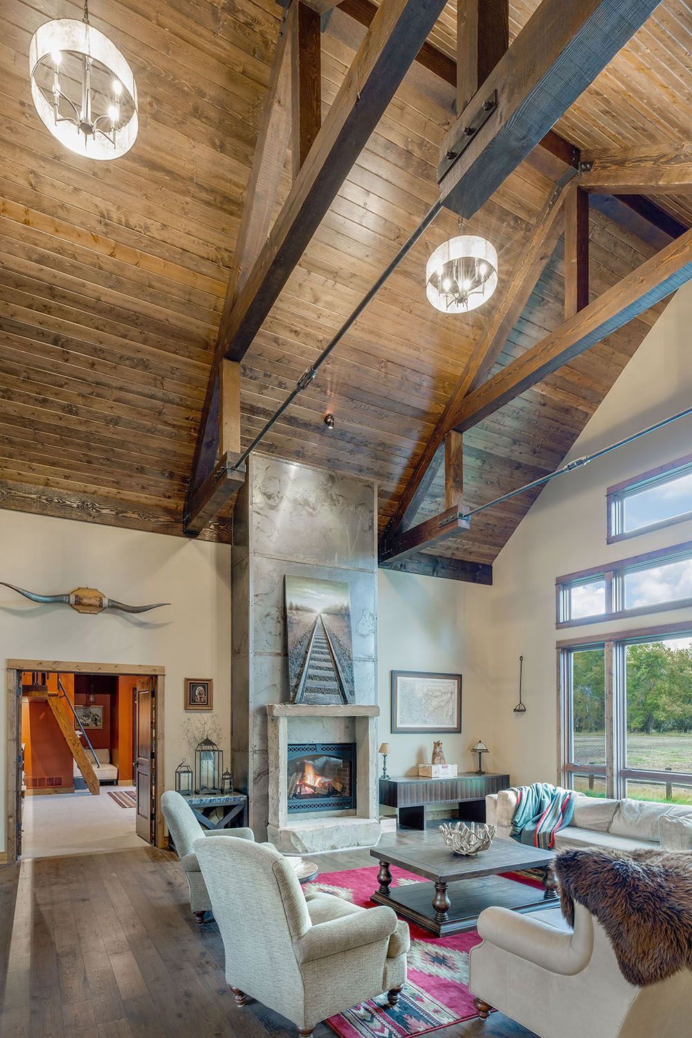 A living room with a stone fireplace, vaulted wood-plank ceiling, exposed timber beams, and comfortable seating
