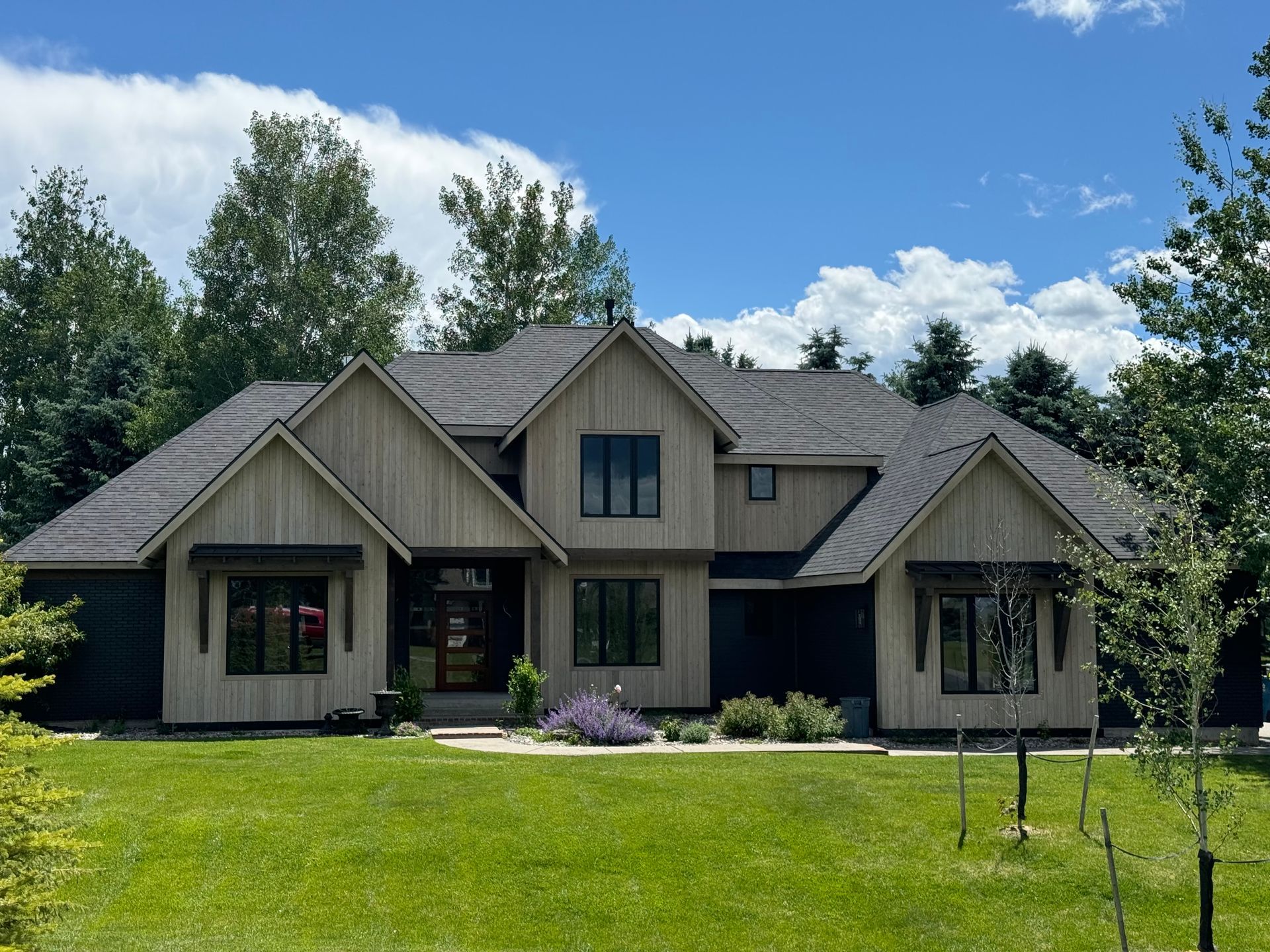 A modern house garage with two black doors featuring side windows, set against a wooden-paneled upper wall and dark siding.