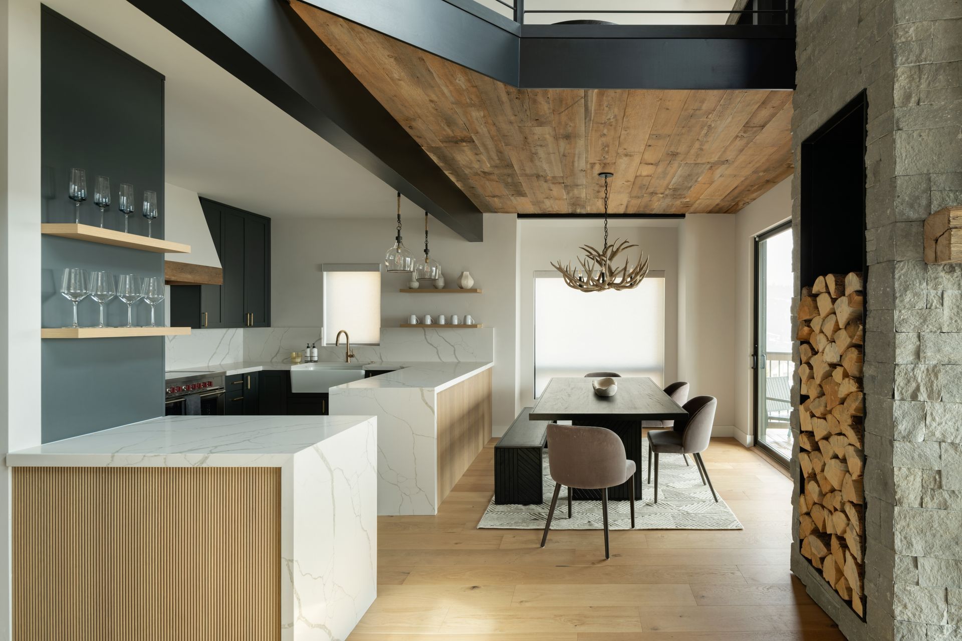 Modern open-concept kitchen and dining area featuring a stone fireplace, wood ceiling, and neutral color palette.