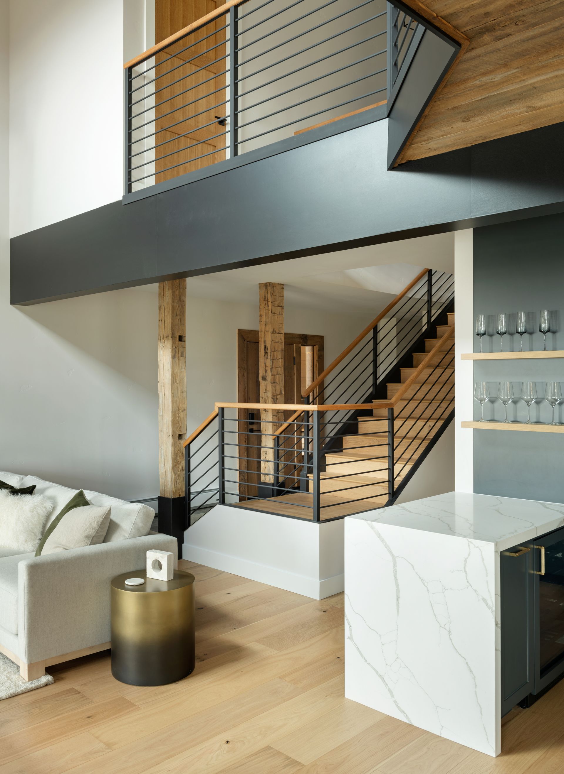 A modern interior showing a living room, a kitchen island with quartz counters, and a wood-accented staircase with railings.