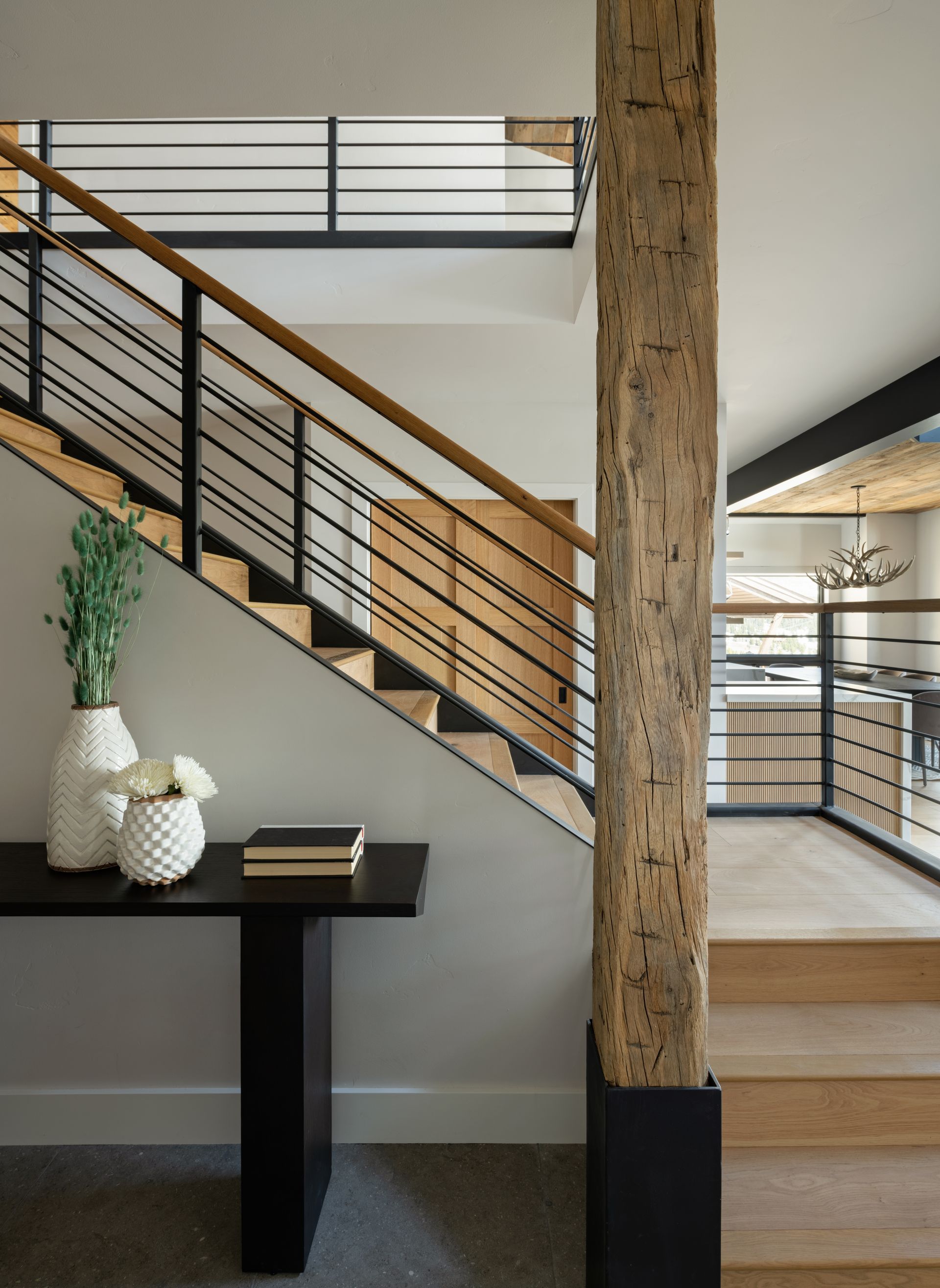 A modern staircase with a black metal railing and wooden treads, beside a textured wooden pillar and a console table.