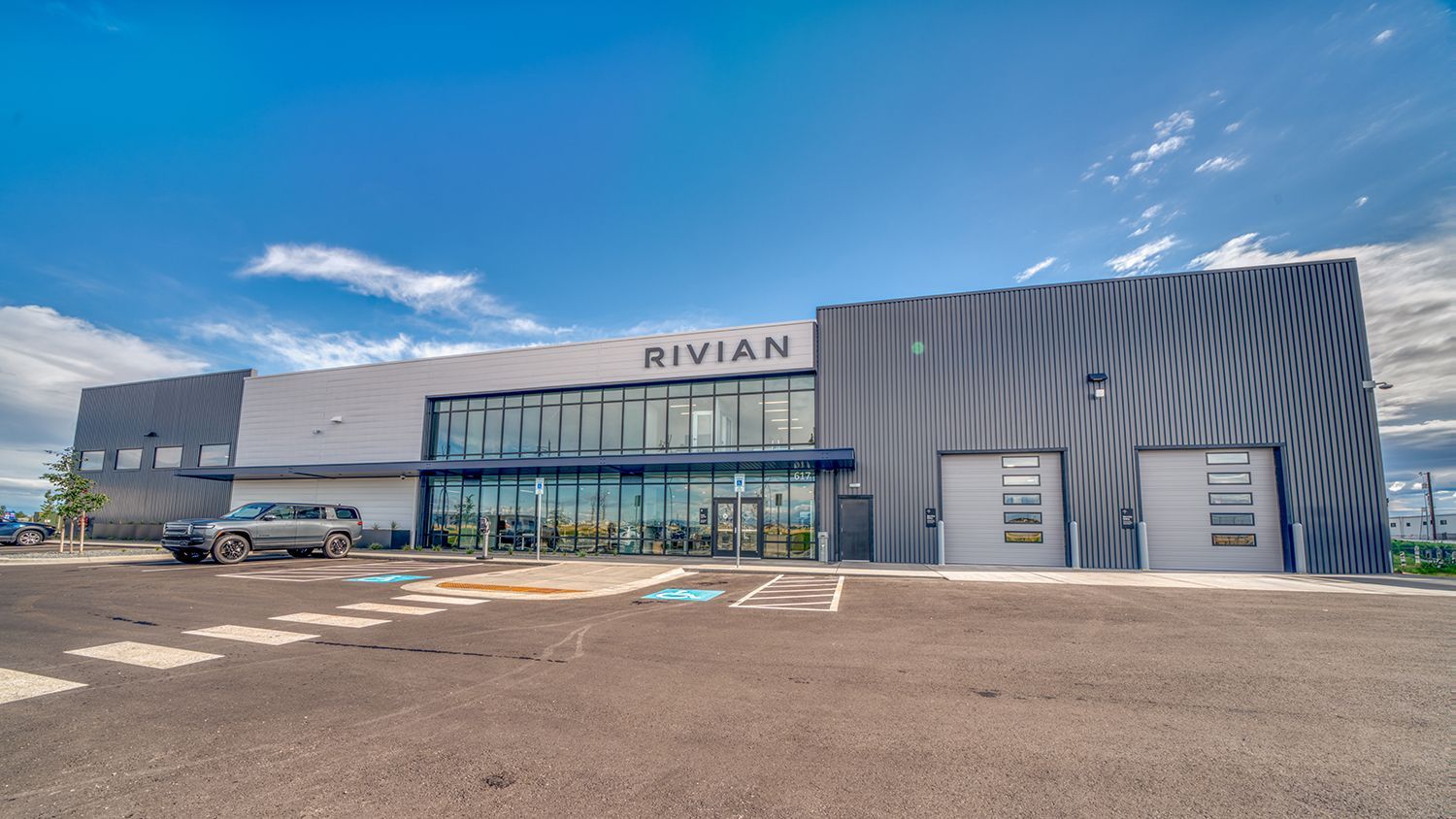 Exterior of a Rivian building with storefront and service bay doors under a blue sky.