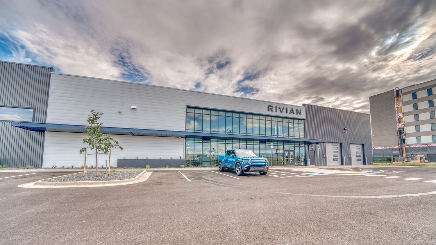 Rivian dealership exterior with blue pickup truck parked out front on a cloudy day.
