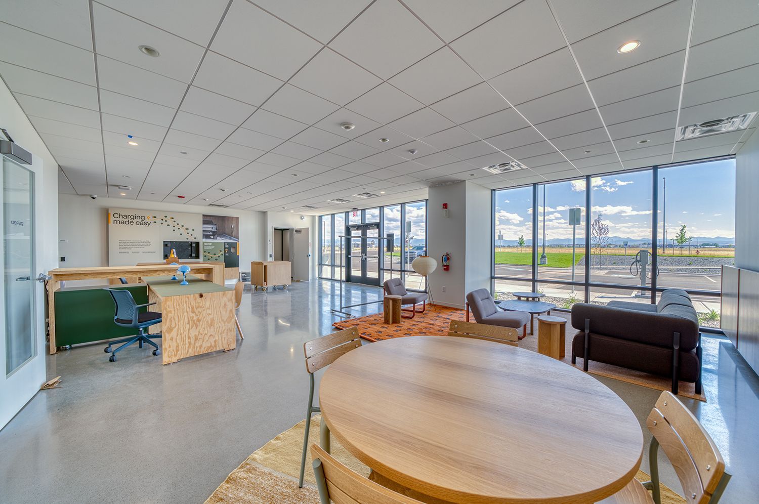 Bright open-plan office space with large windows, round table, chairs, sofa, and modern decor.