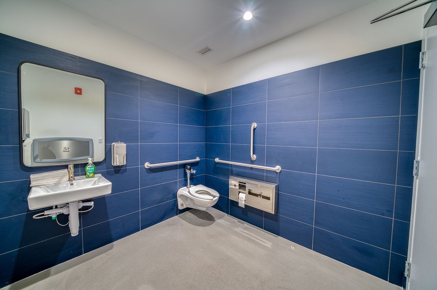 Accessible bathroom with blue tile walls, a toilet, sink, and grab bars.